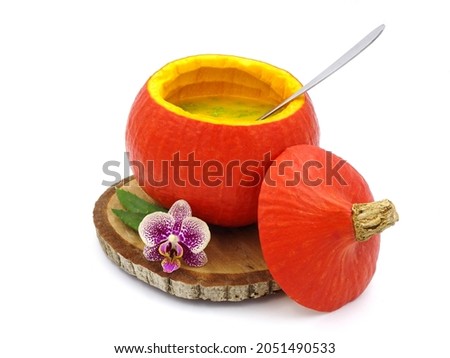 Exotic pumpkin soup in hollowed-out pumpkin on a wooden board with an orchid, on a white background.