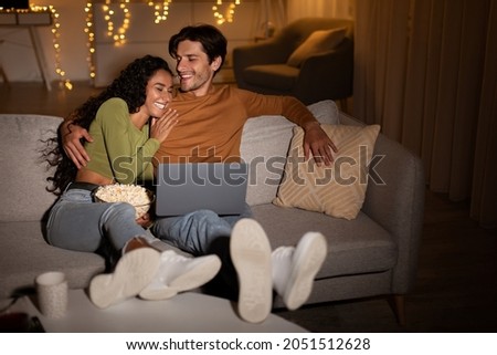 Couple Laughing Watching Comedy Movie On Laptop Online Relaxing And Having Fun Sitting On Sofa At Home At Night. Weekend Leisure And Entertainment Concept. Selective Focus