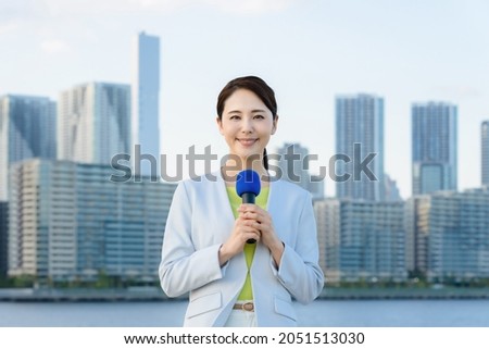 Young asian announcer reporting in front of the city. Royalty-Free Stock Photo #2051513030