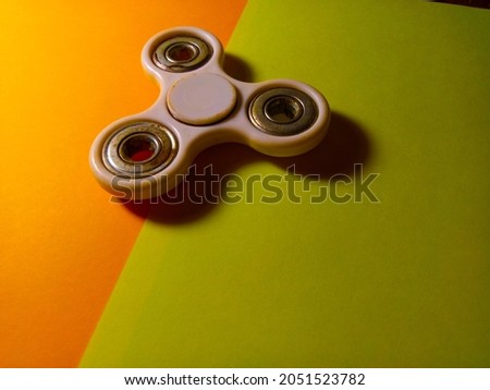 A rusty white fidget spinner on the iron on a yellow and orange origami paper background
