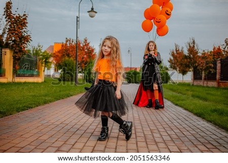 Two young pretty sisters in halloween costumes like witches posing and having fun on the street. Focus is at the youngest girl. Holiday concept. 