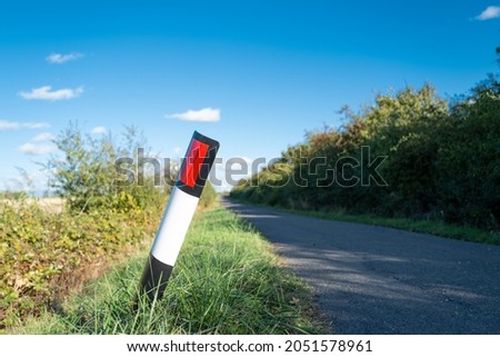 Shallow focus of a bent over, plastic traffic bollard and red reflector seen near a dangerous bend on a narrow country road.