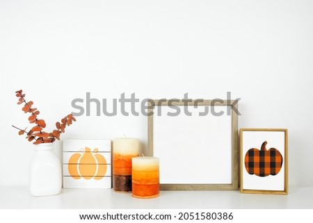 Fall mock up. Wood frame,  wooden pumpkin signs, candles and autumn leaves on a white shelf against a white wall. Modern farmhouse concept. Copy space.