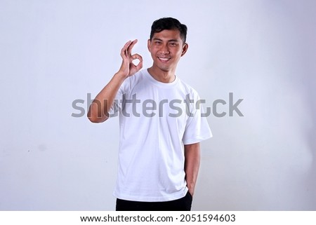 Asian man in white shirt with smiling expression and showing okay symbol using finger. Isolated on a white background