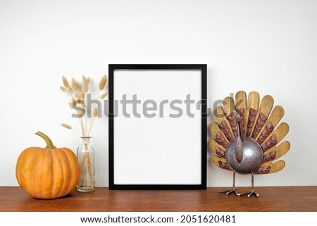 Mock up black frame with thanksgiving turkey, pumpkin and autumn decor on a wood shelf. Fall concept. Portrait frame against a white wall. Copy space.
