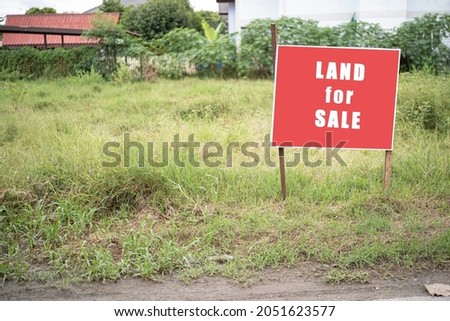 Land for sale sign. Red sign for sale plot. Green lawn behind sign. Land for sale signboard on street signs. Buying plot building a house. signboard of realtor or real estate agent.