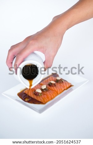 Hand pouring soy sauce on Salmon sashimi on white plate on white background. Isolated on white. Japanese traditional food. Healthy food concept.