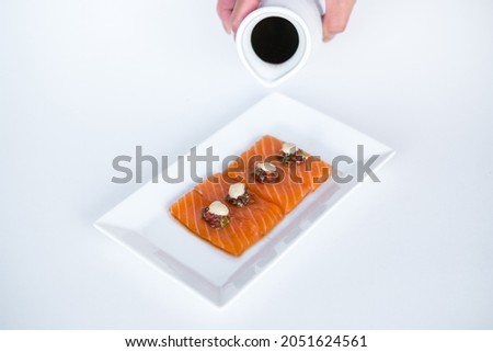 Hand pouring soy sauce on Salmon sashimi on white plate on white background. Isolated on white. Japanese traditional food. Healthy food concept.
