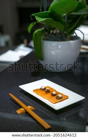 Salmon sashimi on white plate and wooden chopsticks on black table in Japanese restaurant. Japanese traditional food.