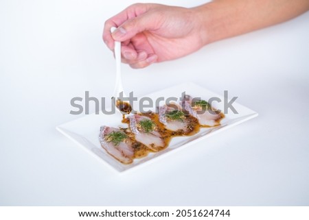 Sea bass sashimi with soy sauce on white plate isolated on white background. Hand pouring sauce on sea bass sashimi. Sushi in Japanese restaurant.