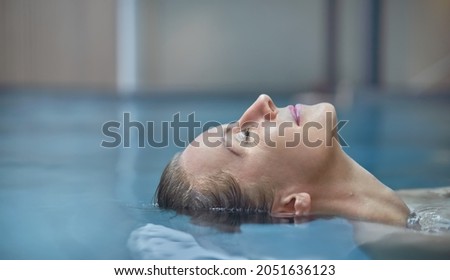 Wellness - happy white woman in her 30s relaxing in wellness resort pool, smiling.