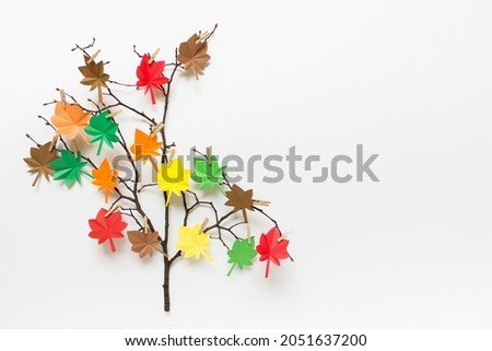 Simple autumn decorative element - dry branch with paper colorful maple leaves on white background. Image with copy blank space.