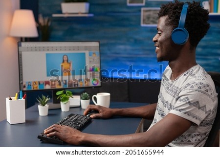 Young african american photographer with headphones retouching designer photography using digital post production software. Man illustrator editor editing creative pictures working remote from home