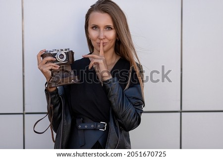 Portrait of a beautiful woman photographer with a retro camera isolated on a grey wall.