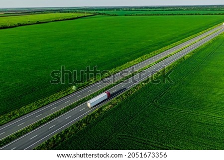 cargo delivery. white truck with red cockpit driving on asphalt road along the green fields. seen from the air. Aerial view landscape. drone photography. 