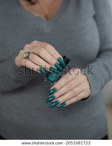 Woman's hands with long nails and turquoise blue green manicure with bottles of nail polish	