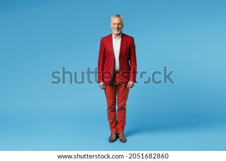 Full length of successful smiling funny elderly gray-haired mustache bearded business man wearing red jacket suit standing and looking camera isolated on blue color wall background studio portrait Royalty-Free Stock Photo #2051682860