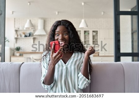 Young African girl at home reading message on mobile phone on unexpected news, happy client winning online shopping promo, gets prize in social media giveaway. Good luck big win concept. Royalty-Free Stock Photo #2051683697