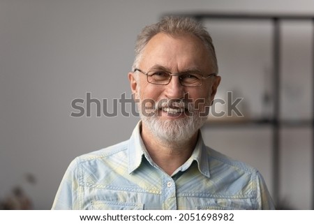 Head shot portrait of happy mature old retired man in eyewear posing indoors. Emotional smiling elderly senior hoary grandfather looking at camera, enjoying communicating distantly by video call. Royalty-Free Stock Photo #2051698982
