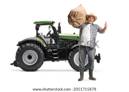 Full length portrait of a happy mature farmer gesturing thumbs up in front of a tractor isolated on white background