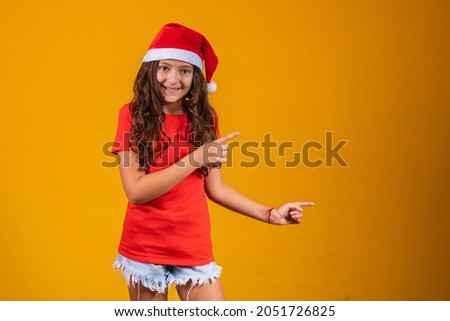 portrait of a little girl dressed in Christmas outfit pointing to free space for text.