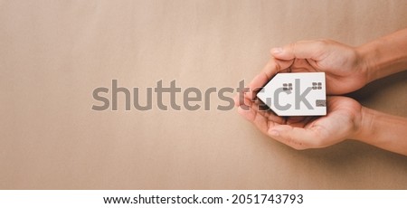 Woman hand holding white house, homeless housing and home protecting insurance concept, international day of families, homeschooling, Top view.
