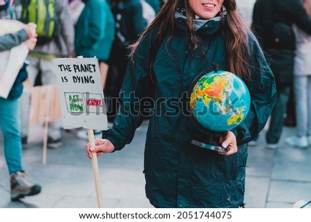 Women holds a globe of earth and a banner with phrase " The planet is dying. Act now. Ignore. Choose. Environment. Nature. Protest. Crowd. Street. Agreement