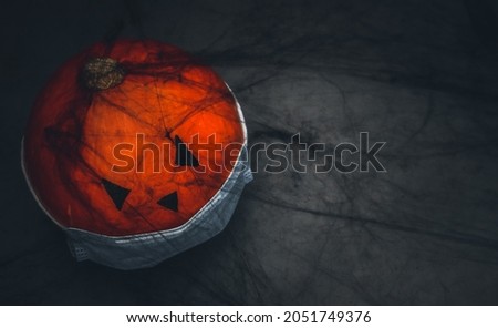 A pumpkin with a painted face in a medical mask and a black spider web lie on the left against a gray background with space for text on the right, top view close-up. Halloween coronavirus concept .