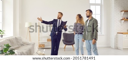 Realtor giving future tenants or first time buyers tour about modern apartment. Boyfriend and girlfriend or husband and wife planning to buy new home and meeting with real estate agent in new house Royalty-Free Stock Photo #2051781491