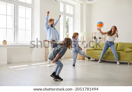 Happy family having fun at home all together. Mother, father and children playing football in modern living room. Mommy playing as goalkeeper while daddy and little kids are kicking toy soccer ball Royalty-Free Stock Photo #2051781494