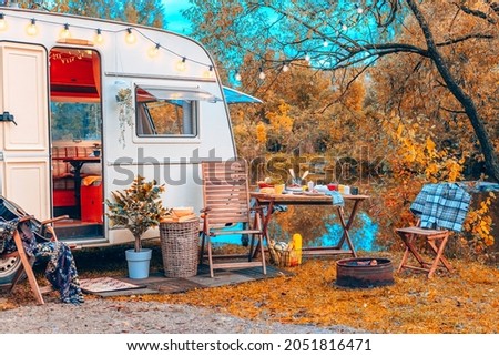 trailer of mobile home or recreational vehicle stands on shore of pond in camping in autumn near table set, concept of family local travel in native country on caravan or camper van and camping life Royalty-Free Stock Photo #2051816471
