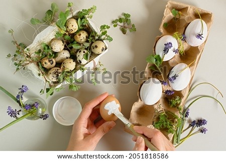 Easter eggs aesthetics of still life. Festive Easter composition in neutral tones. Stylish flat lay of blades of grass, flowers on a gray background. Happy Easter. Drawing by the artist on the eggs