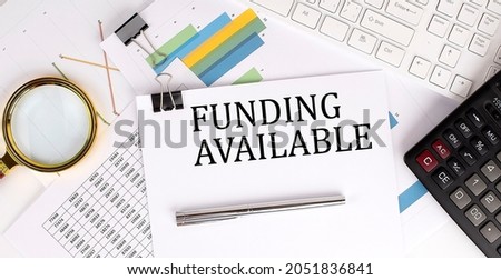 FUNDING AVAILABLE text on the white paper on light background with charts paper ,keyboard and calculator