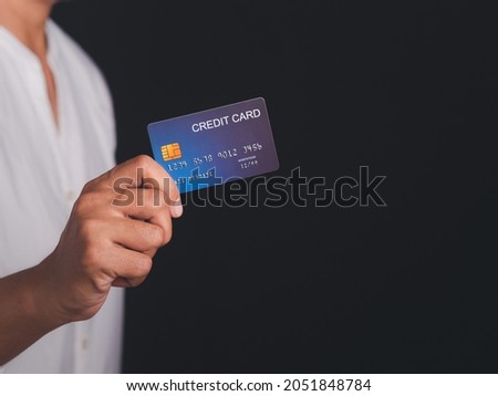Midsection of a businessman in a white shirt holding a mockup blue credit card while standing with a black background in the studio. Close-up photo. Space for text. Money and business concept.