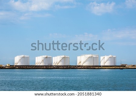 Large white storage tanks for oil and fuel in a marine oil terminal under a blue sky. Royalty-Free Stock Photo #2051881340