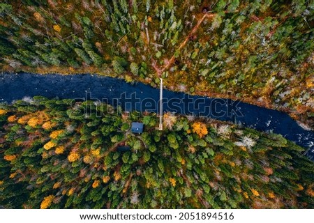 Aerial view of fall forest and blue river with bridge in Finland. Beautiful autumn landscape.