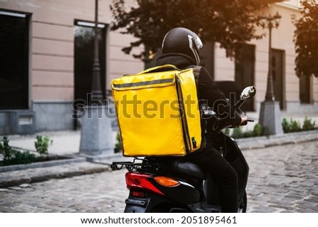 a delivery man rides a moped down the street with an online order. food delivery from the restaurant and shop. Royalty-Free Stock Photo #2051895461