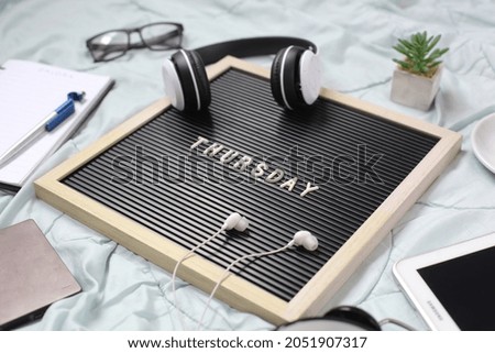 Thursday flat lay concept with multimedia accessories, books and pens, glasses, alarm clock, flowers and coffee for refreshment on white background Royalty-Free Stock Photo #2051907317
