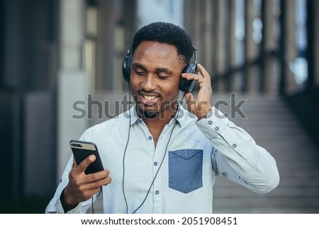 young african student listening to music from smartphone using big headphones, smiling from the convenience of using the app