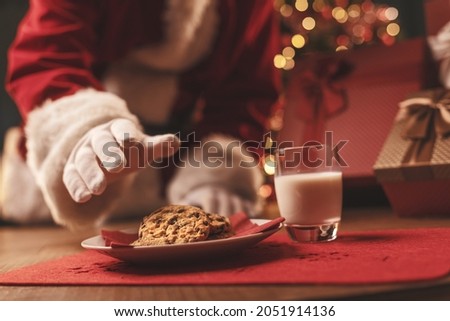Santa Claus having a delicious snack, he is eating cookies and drinking milk, Christmas and holidays concept