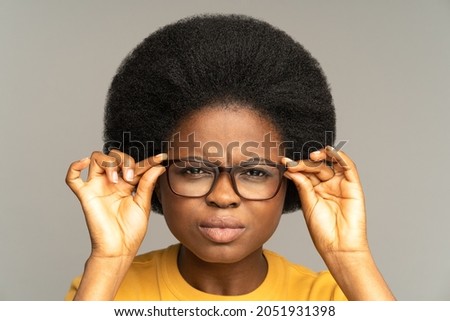 Young african woman with poor eyesight squinting eyes looking through eyeglasses try to read text. Black female in glasses with vision problems winking to focus on small object. Ophthalmology concept Royalty-Free Stock Photo #2051931398