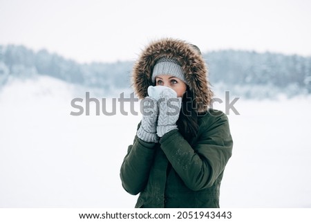 Beautiful young female smiling and drinking tea in nature Winter swimming. Woman in frozen lake ice hole. Swimmers wellness in icy water. How to swim in cold water Gray hat and gloves swimming clothes