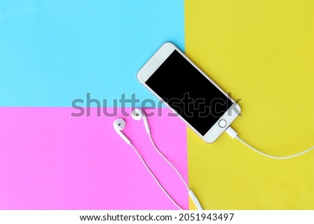 Smartphone with headphones on yellow, purple and blue background, top view.