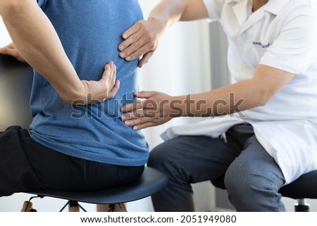 The doctor is diagnosing the patient's back pain. A male with back pain sees a doctor for treatment. Royalty-Free Stock Photo #2051949080