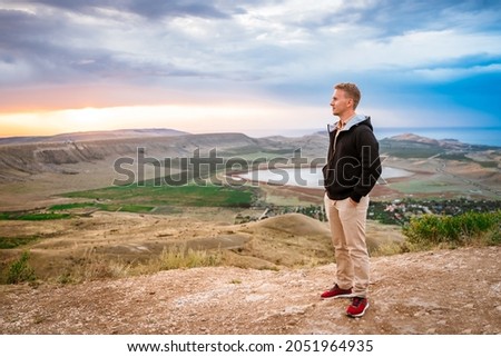 A young man conquered the top of the mountain at dawn. Beautiful mountain landscape with a slope. The concept of enjoying nature.