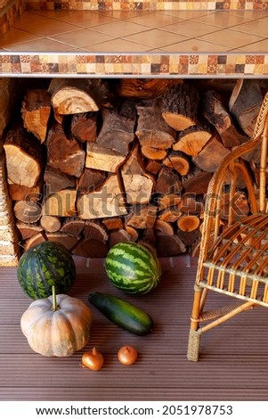 Autumn on the veranda. Two striped watermelons and an orange pumpkin lie on the veranda floor. Next to it is a long zucchini and onions. On the side there is a rattan wicker chair