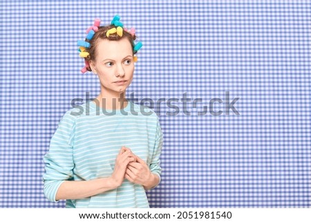 Portrait of thoughtful young woman without makeup with colorful hair curlers on head, looking melancholic and dreamy, standing over shower curtain background, with place for your text and design Royalty-Free Stock Photo #2051981540