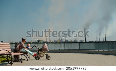 Woman with baby sitting on a bench in a polluted city. environmental pollution and bad ecology in city concept. Ukraine Zaporizhzhia Royalty-Free Stock Photo #2051999792