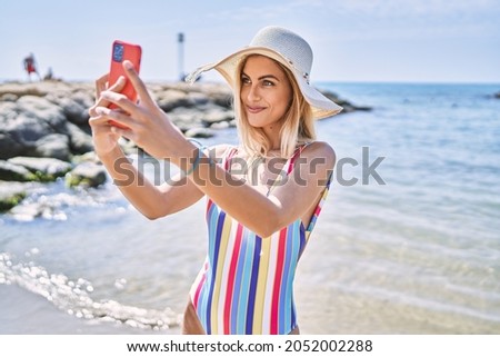 Young blonde girl wearing summer hat making selfie by the smartphone at the beach.