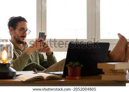 Medium shot of male texting while studying with feet on the desk Royalty-Free Stock Photo #2052004805